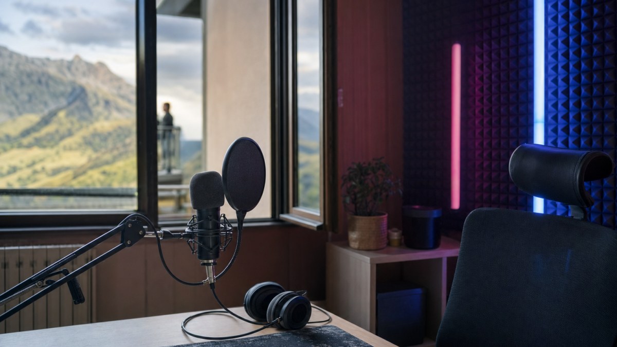 Set de streaming vacío en una habitación, con micrófono de brazo, luces de colores y una ventana que da a las montañas